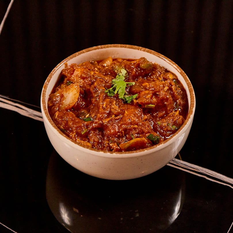 A bowl of rich, red Indian curry with chicken and vegetables, garnished with fresh cilantro.