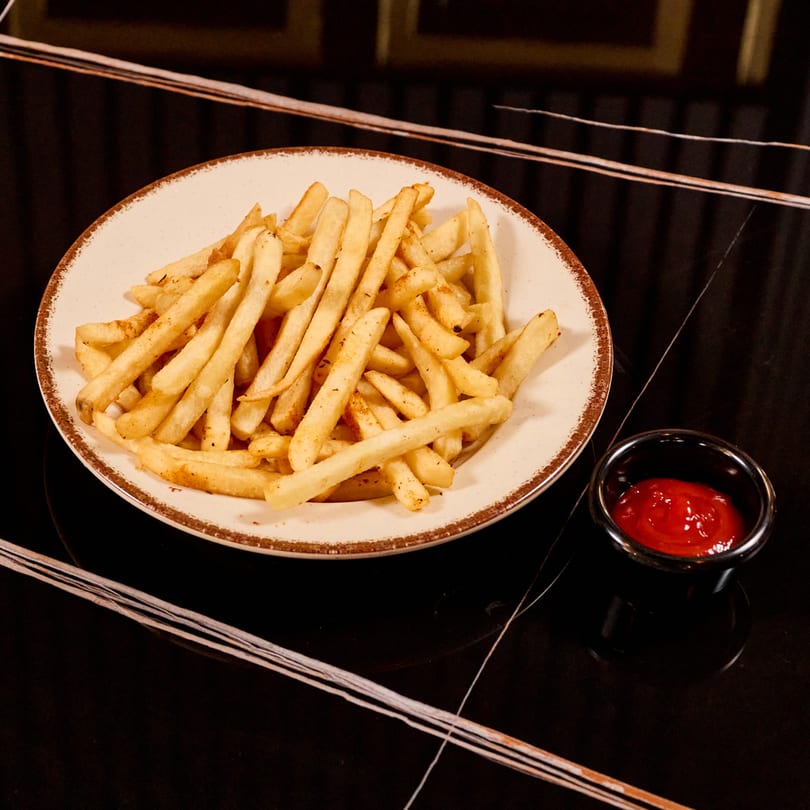 A plate of golden french fries with a side of ketchup on a dark, reflective table.