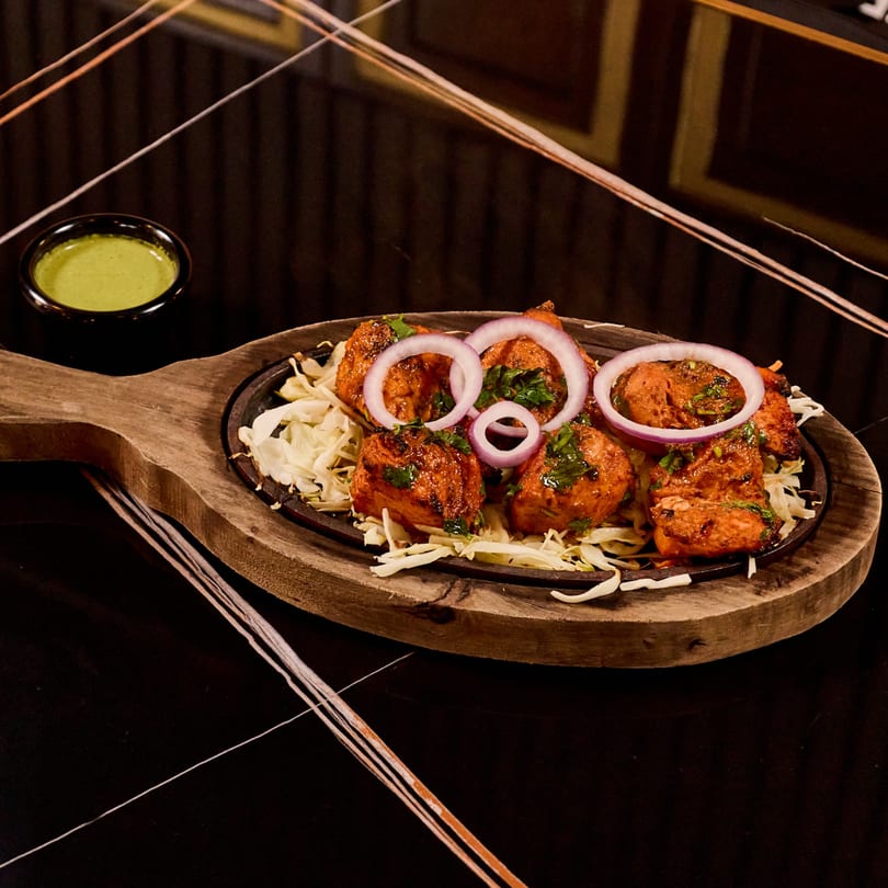 Indian chicken tikka with red onion and cabbage on a sizzling platter with green chutney.