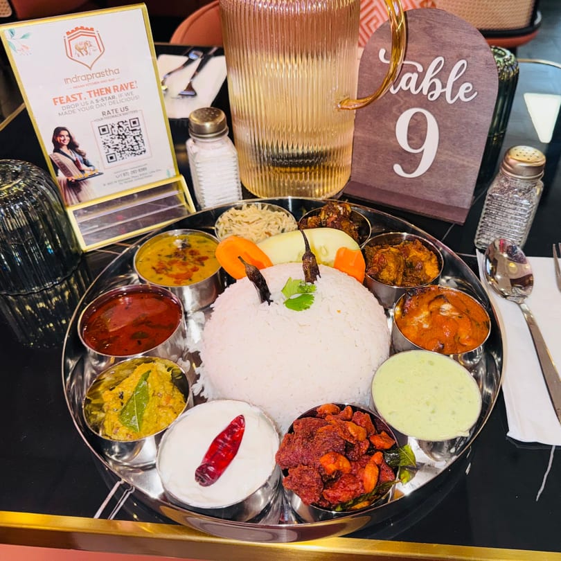 Indraprastha Indian Kitchen's thali with rice, curries, and sides, alongside a table number and water.