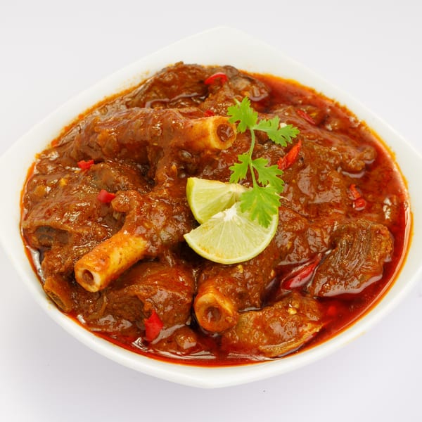 Indraprastha Indian Kitchen's rich, red Indian curry with meat on the bone, garnished with lime and cilantro.